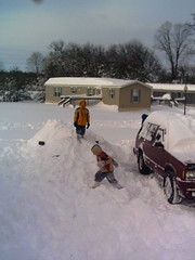 two young boys playing on a car buried in a snowdrift